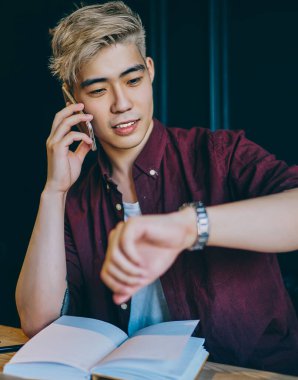 Şık sarışın hippi öğrenci akıllı telefondan ararken saati kontrol ediyor ve arkadaşlarıyla konuşuyor. Genç adam cep telefonuyla iletişim kurarken kol saati yönetiyor.