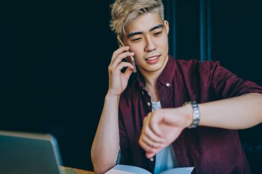 Şık sarışın hippi öğrenci akıllı telefondan ararken saati kontrol ediyor ve arkadaşlarıyla konuşuyor. Genç adam cep telefonuyla iletişim kurarken kol saati yönetiyor.