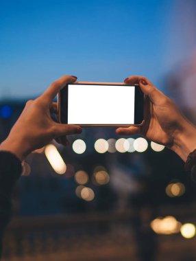 Tanımlanamayan kadın fotoğrafçı elinde modern cep telefonuyla boş ekrana bakarak şehrin gece fotoğraflarını çekiyor.