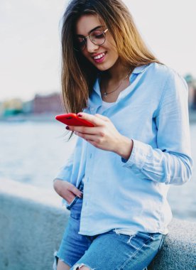 Gündelik kıyafetlerle gezen genç kadın gezgin şehir ortamında akıllı telefondan sohbet ediyor. Neşeli hipster blogcu, cep telefonundan bildirimi okuyor.