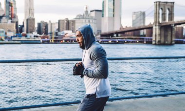 Ciddi bir atletik etnik dövüşçünün kentteki nehir kenarındaki sette modern rahat spor kıyafetleriyle antrenman yapmasının yan görüntüsü.