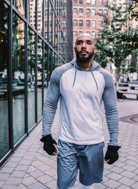 Spor kıyafetleri içinde kulaklıkları olan güçlü Afrikalı Amerikalı bir adam modern ofis binasının yakınındaki bir sokakta antrenman yaparken gözlerini kaçırıyor ve yürüyor.