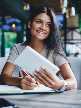 Kafeteryadaki uzak iş için dijital tablet ve wifi kullanan neşeli, güzel kadın blogcu, taşınabilir bilgisayar taşıyan not defterinde iş planlama bilgisi olan başarılı kadın.