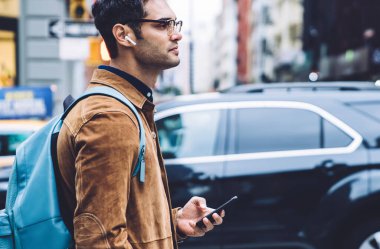 Gözlüklü, kahverengi süet ceketli, sırt çantalı ve kulaklıklı, müzik dinleyen ve New York 'ta dolaşırken düşünen meditasyon yapan yakışıklı bir erkek.