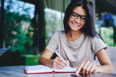 Kafkasyalı olumlu kadın cep telefonundan bildirimi kontrol ederken not defterine bilgi yazıyor, neşeli genç bayan blogcu takipçilerle akıllı telefon aracılığıyla sohbet ediyor ve kafede makaleler yaratıyor.