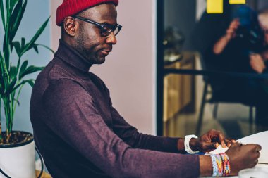 Sıradan giyinen Afrikalı Amerikalı hipster 'ın yan görünüşü birlikte çalışma ofisindeki planlama projesi için yazma bilgisi, zeki ciddi erkek öğrenci işletme okulunda öğrenmeye odaklandı.