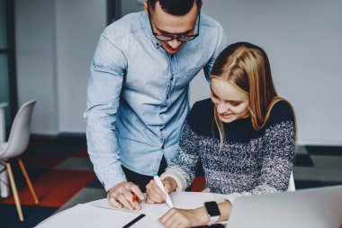 Masaüstünde dizüstü bilgisayarla oturan ve erkek öğretmenle işbirliği yapan olumlu genç kadın çizimi. Modern ofiste mimari proje üzerinde çalışan iki genç iş arkadaşı.