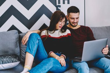 Genç evlilik rahat bir kanepede dinleniyor ve modern dizüstü bilgisayarda sosyal ağda komik videolar izliyor birlikte boş zaman geçiriyorlar, aşık çift internet üzerinden alışveriş yapıyor kablosuz internet kullanarak