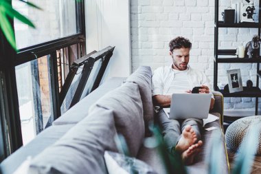 Ciddi bir beyaz adam internetten internet üzerinden ödeme yapmak ve alışveriş yapmak için dizüstü bilgisayar kullanıyor. Hippi adam oturma odasında elinde netbook ile evde boş zamanlarında video seyrediyor.