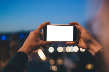 Tanımlanamayan kadın fotoğrafçı elinde modern cep telefonuyla boş ekrana bakarak şehrin gece fotoğraflarını çekiyor.
