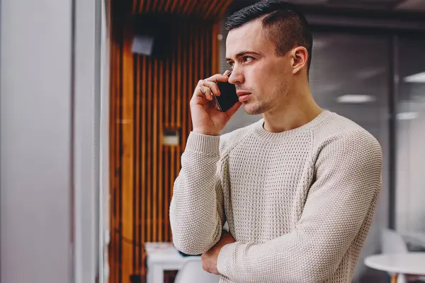 Sıradan giyinmiş, iş meselelerini çözen ciddi bir genç adam. Akıllı telefon görüşmeleri sırasında ofiste durup pencereden dışarı bakıyor. Cep telefonundan kendine güveni tam bir erkek yönetici arıyor.