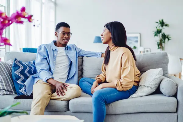 Dark skinned male and female hipsters having positive conversation resting at home interior together, african american couple in love talking about relationships at modern designed apartment