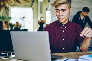 Düşünceli Asyalı hippi öğrenci modern laptop aygıtında kablosuz internet kullanarak internet üzerinden özel ders izliyor. Çinli genç adam dijital netbook üzerinde web sayfası tasarımı üzerinde çalışıyor.