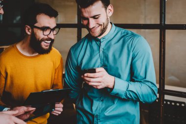 Modern akıllı telefondan komik videolar izlerken gülen olumlu arkadaşlar cihazda 4G internet kullanıyorlar. Neşeli hipster çocuklar telefon cihazında haberlerin tartışılması sırasında eğleniyorlar.