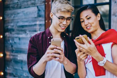 Olumlu Çinli hipster çocuklar, şehir ortamında 4G internet üzerinden modern akıllı telefondan komik videolar izlerken gülüyorlar. Neşeli arkadaşlar cep telefonları kullanarak ağlarda medyayı paylaşıyorlar.