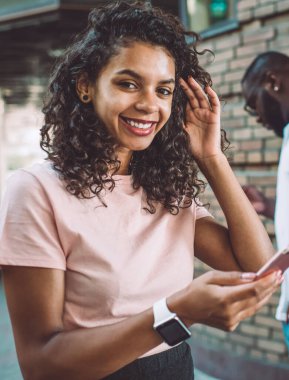 Elinde cep telefonu cihazıyla kameraya gülümseyen güzel kıvırcık saçlı Afro-Amerikan hippi kızın yarım boy portresi. Milenyum insanları kavramı.