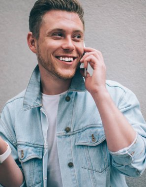 Kot ceketli yakışıklı bir adam ve akıllı bir saat sokakta durup mutlu bir şekilde gülümserken telefonda mutlu bir şekilde el kol hareketi yapıyor.