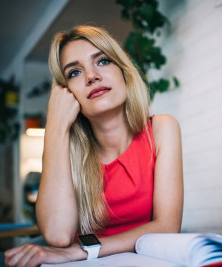 Düşünceli sarışın kız öğrenci kitaplarla masada oturuyor ve kafeteryada çalışırken tatilin hayalini kuruyor ve ödev yapıyor.