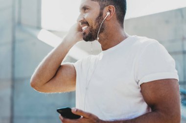 Boş tişörtlü, mutlu ve mutlu bir adamın bakışları. Motivasyon konsepti olan sesli kitapları dinlerken gülümsemesi. Elektronik kulaklıklı neşeli bir erkek.