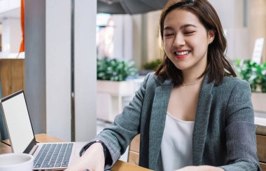 Ofis kıyafetleri içinde gülümseyen güzel bir bayan cep telefonu işyeri merkezindeki kafede dizüstü bilgisayarla oturuyor ve belgeleri düzenliyor.