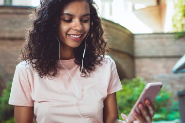 Elektronik kulaklıklı mutlu koyu tenli hipster melodisi internet arkadaşlarıyla çevrimiçi iletişimde iyi hissediyor ve popüler müzik parçaları olan favori müzik podcast 'ini dinleme zamanı.