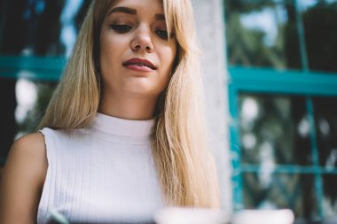 Beyaz kolsuz balıkçı yaka giyen ve sundurmada otururken dizüstü bilgisayara bakan sarışın bir kadın.