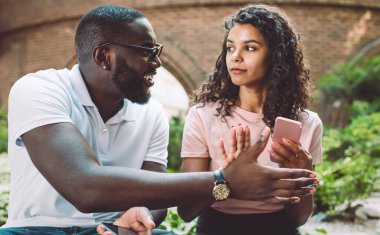 Kıvırcık saçlı Afro-Amerikalı hippi kız kıskanç erkek arkadaşından akıllı telefon aygıtı saklıyor ihanetinden şüpheleniyor online sohbet, ilişki kavramı ve aşk sırlarını okumaya çalışıyor.