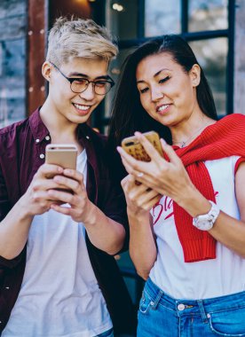 Olumlu Çinli hipster çocuklar, şehir ortamında 4G internet üzerinden modern akıllı telefondan komik videolar izlerken gülüyorlar. Neşeli arkadaşlar cep telefonları kullanarak ağlarda medyayı paylaşıyorlar.