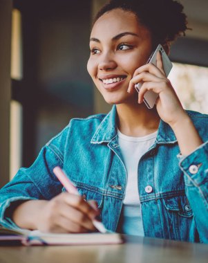 Mutlu siyahi kız öğrenci otokopi için eğleniyor ve sınava hazırlanırken akıllı telefon uygulamasını kullanarak arkadaşını arıyor, başarılı hipster kız cep telefonuyla konuşuyor.