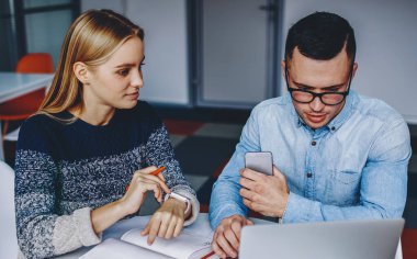 Gündelik kıyafet giyen iki öğrenci dizüstü bilgisayarlarında ders izliyorlar ve modern ofiste not defteriyle birlikte oturuyorlar. Genç adam ve kadının işbirliği ile ortak çalışma projesi hazırlıyorlar.