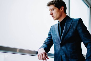 Resmi olarak giyinmiş düşünceli yakışıklı erkek yönetmen çatı katındaki pencereye bakarak gelecek planlarını düşünüyor. Zarif takım elbiseli, düşünceli, kendine güvenen beyaz iş adamı iş için fikirlere odaklanıyor.