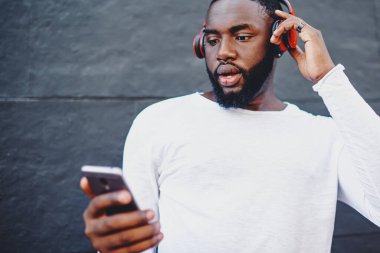 Erkek meloman içerik sitesinde yeni ses şarkıları arıyor. Uygulama fiyatından şok olmuş hissediyor. Bluetooth kulaklıkla sesli kitap dinlemek için cep telefonuyla sohbet eden adam.