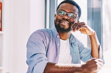 Siyah gülümseyen entellektüel düşünceli yazar, güneşli odada kalem ve defterle otururken kompozisyon yazıyor.