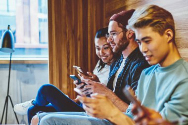 Çağdaş teknoloji düşkünü genç nesil hipsterler online sohbet ve ağ kurma bağımlısı, pozitif çok ırklı erkek ve kadınlar akıllı telefonlarla birlikte otururken iletişimi görmezden geliyorlar.