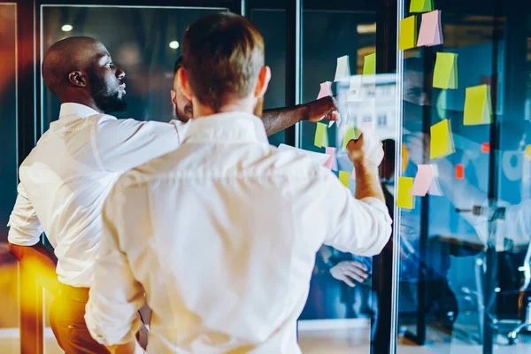 African american proud ceo pointing on colorful stickers with notes glued on glass wall during collaboration on successful project.Cooperation between proud ceo and employees in modern office