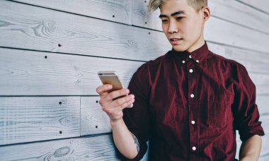 Düşünceli Asyalı hippi adam elinde akıllı telefonu tutuyor ve birlikte çalışırken duvarın yanında duran akıllı telefondan gelen mesajı okuyor. Çinli genç adam cep telefonuyla 4G internet kullanıyor.