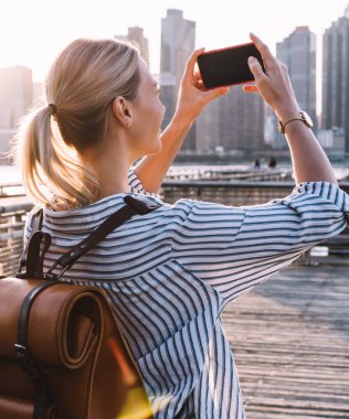 Milenyum kadınlarının gelişigüzel çekilmiş fotoğraflarının arka planında New York manzarasının çekim videosu çekiliyor. Fotoğraf çekmek için akıllı telefon ana kamerası kullanılıyor. Kadın turist cep telefonlarını test ederken şehrin fotoğraflarını çekiyor.
