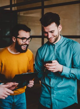 Modern akıllı telefondan komik videolar izlerken gülen olumlu arkadaşlar cihazda 4G internet kullanıyorlar. Neşeli hipster çocuklar telefon cihazında haberlerin tartışılması sırasında eğleniyorlar.