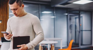 Milenyum genç işadamı elinde not defteriyle akıllı telefondan finansal haberler okuyor modern ofiste ücretsiz 4G internet bağlantısı kullanıyor. Cep telefonundan e-postayı kontrol eden düşünceli öğrenci.