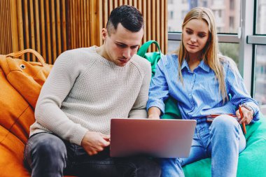 Gündelik giyinmiş genç bir adam ve kadın rahat bir nonoşun üzerinde oturmuş modern bir dizüstü bilgisayarda internet üzerinden film izliyorlar. Moda ortamında ücretsiz kablosuz internet bağlantısı kullanıyorlar.