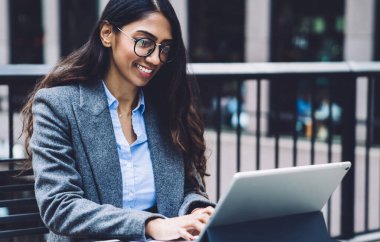 Uzun saçlı, gözlüklü, teras masasında oturan, gazete ve tabletlerle çalışan neşeli, modern etnik kadın.
