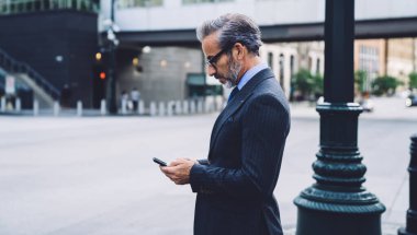 Yetişkin modaya uygun iş adamının New York 'ta kaldırımda dikilirken telefon dinlemesi bulanık arka planda.