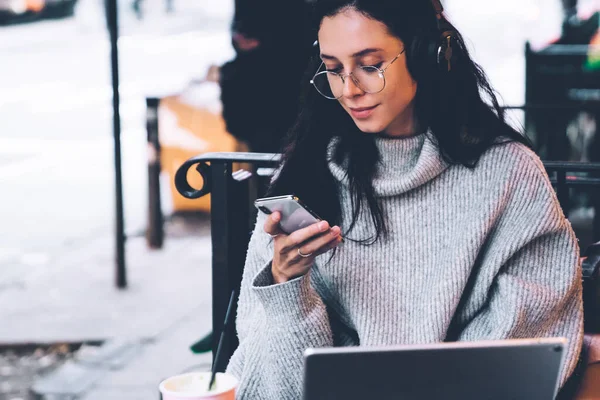 Gözlüklü, kulaklıklı, akıllı telefonlu, modern tabletli modern New York 'un kafe terasında oturan genç ve güzel bir bayan.