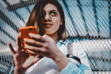 Akıllı telefonu elinde tutan ve yüksek hızlı umumi internet bağlantısı üzerinden cihaza uygulama yükleyen genç bir kadının bakış açısının altında. Hipster kızı cep telefonuyla internet üzerinden ödeme yapıyor.