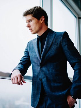 Resmi olarak giyinmiş düşünceli yakışıklı erkek yönetmen çatı katındaki pencereye bakarak gelecek planlarını düşünüyor. Zarif takım elbiseli, düşünceli, kendine güvenen beyaz iş adamı iş için fikirlere odaklanıyor.