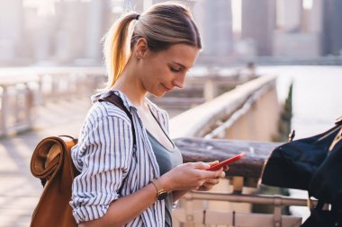 Sırt çantasıyla gezen beyaz kadın turistin yan görüntüsü. Konum bilgilerini kontrol ederken akıllı telefon uygulaması olan GPS 'leri takip ediyor ve New York - New York çevresinde online rehber arıyor.