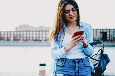 Şehirdeki kentsel ortamlarda duran modern akıllı telefon cihazıyla ilgili gelen uyarıyı okuyan çekici genç kadın. Ücretsiz 4G internet bağlantısı kullanarak uygulamayı güncelleyen kadın blogcu.