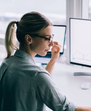 Modern ofisin penceresinin yanında bilgisayar ve tabletle çalışan çağdaş, zeki iş kadınının yan görünüşü