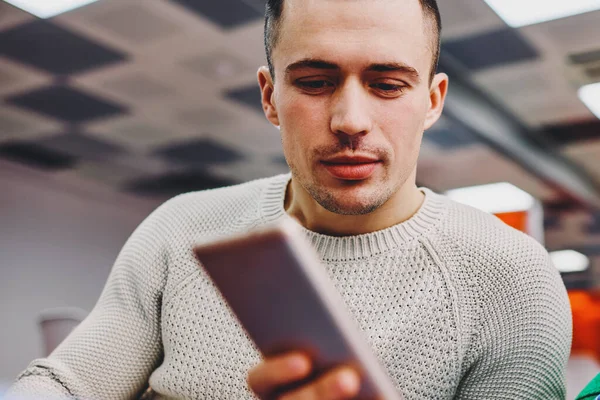 Young man dressed in casual wear watching video in social networks on modern smartphone device.Hipster guy reading email with notification on digital cellular using 4G internet connection
