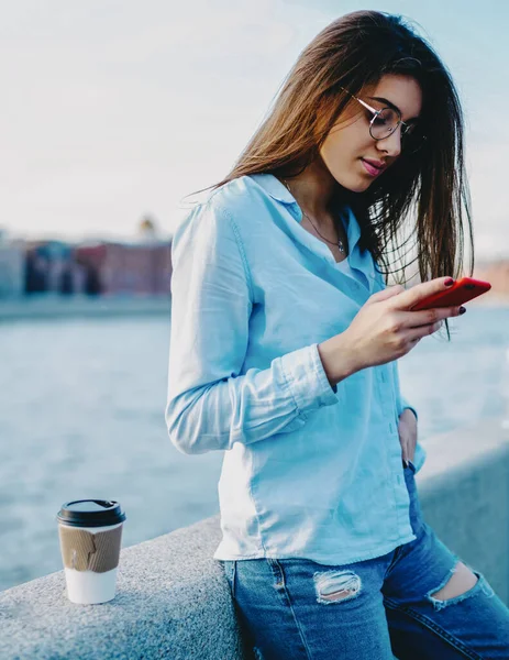 Charming casual dressed young woman enjoying trip and chatting in social networks with followers on smartphone device using 4G internet.Hipster girl reading received message on mobile phone